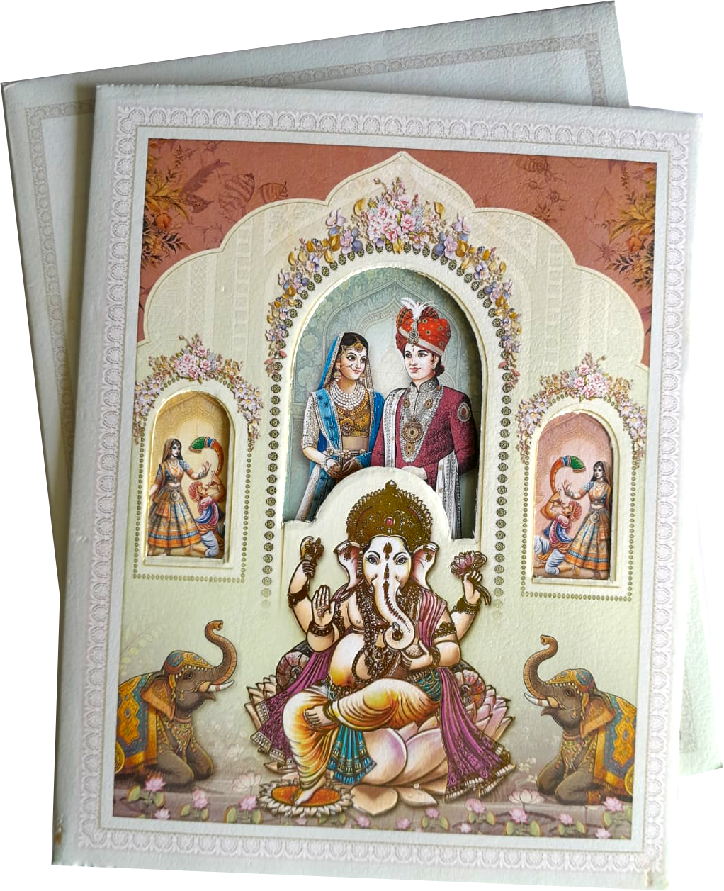 Traditional temple architecture with floral borders, an arched window frame for the couple, and a seated Lord Ganesha. — wedding invitation card